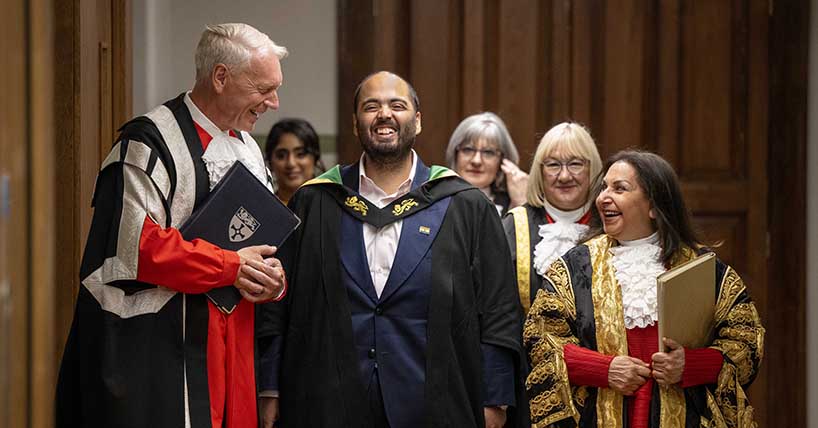 Procession exiting ceremony with participants in red, black and gold University gowns and Professors Ambani, Day laughing with Chancellor Imtiaz Dharker